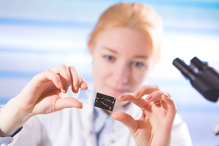 woman in a laboratory microscope with microscope slide in hand